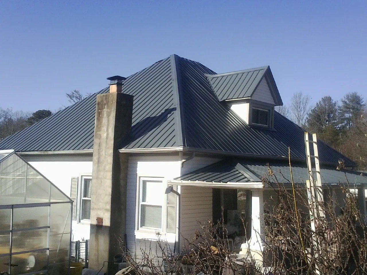 Dark blue standing seam metal roof on a white farmhouse with dormer — Slate & Tile Roof Repair by Roofing Brothers in Bogart