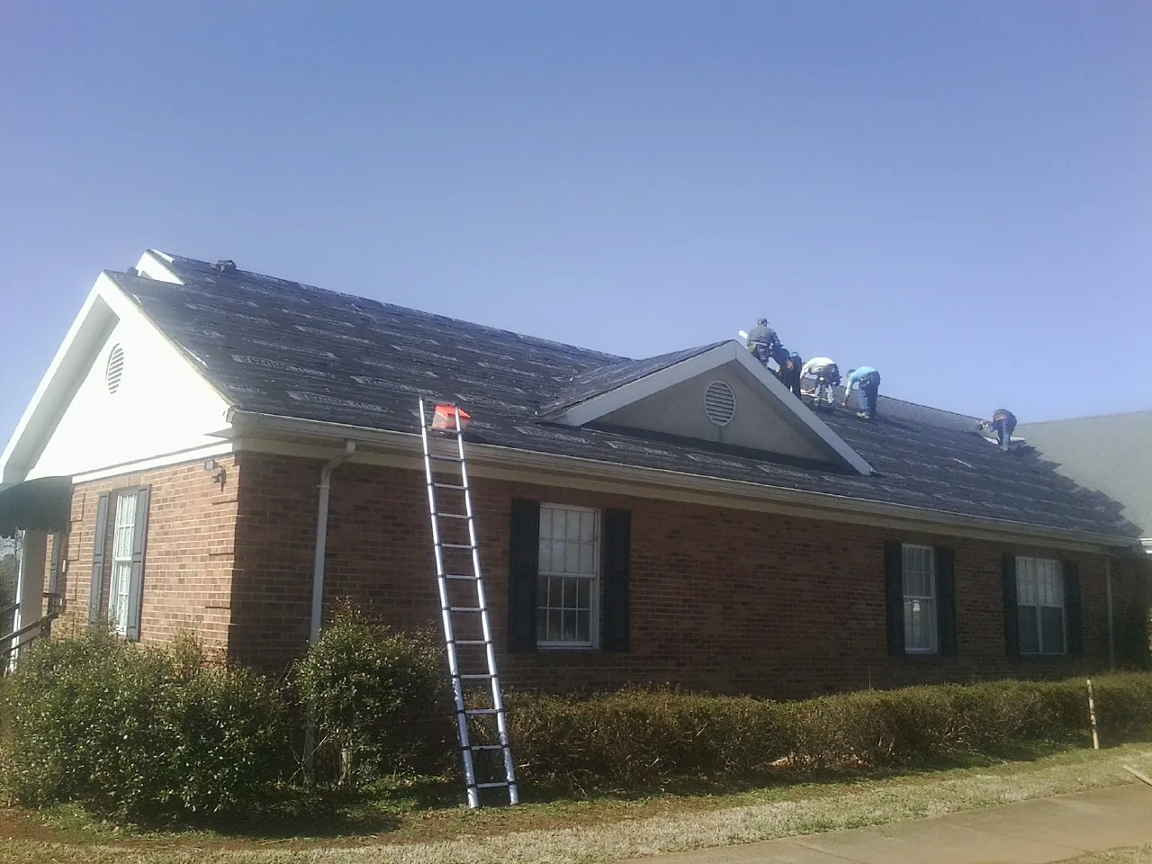 Crew tearing shingles off a brick ranch roof with a ladder set — Metal Roof Repair work by our crew in Bogart