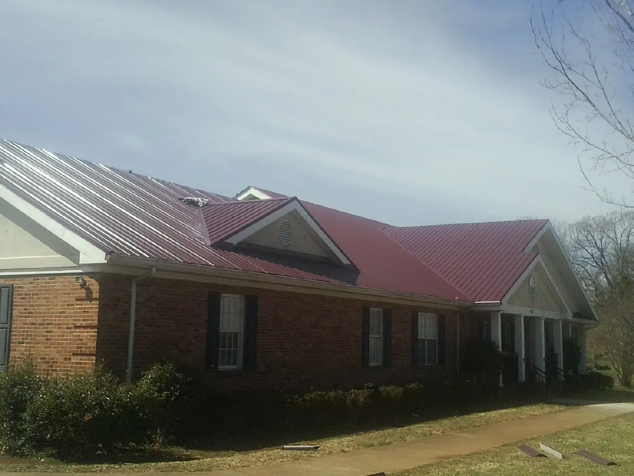 Red metal roof with gabled entries on a long brick building, from a Hail Damage Roof Repair job in Bogart