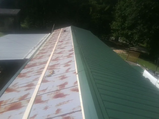 Old rusted panels beside newly installed green metal roofing — Wind Damage Roof Repair by Roofing Brothers in Bogart