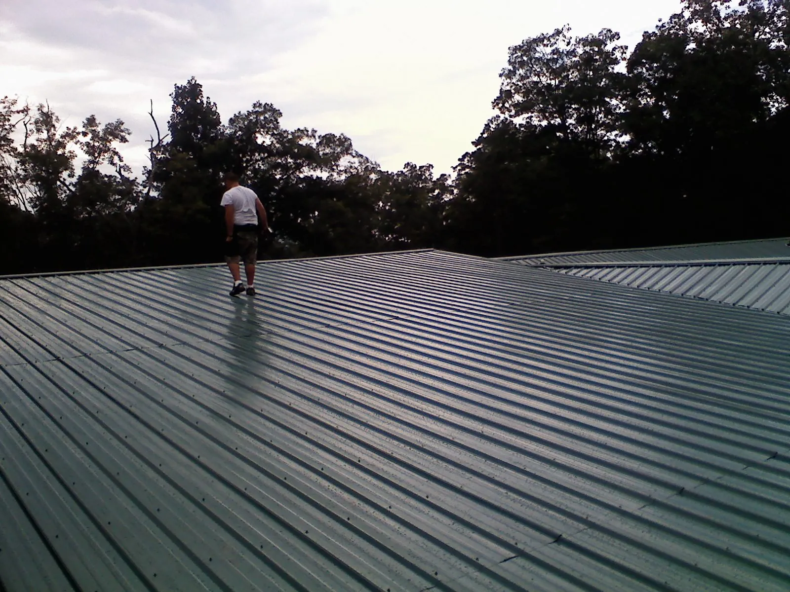 Roofer walking a wide expanse of new green metal roofing in Bogart