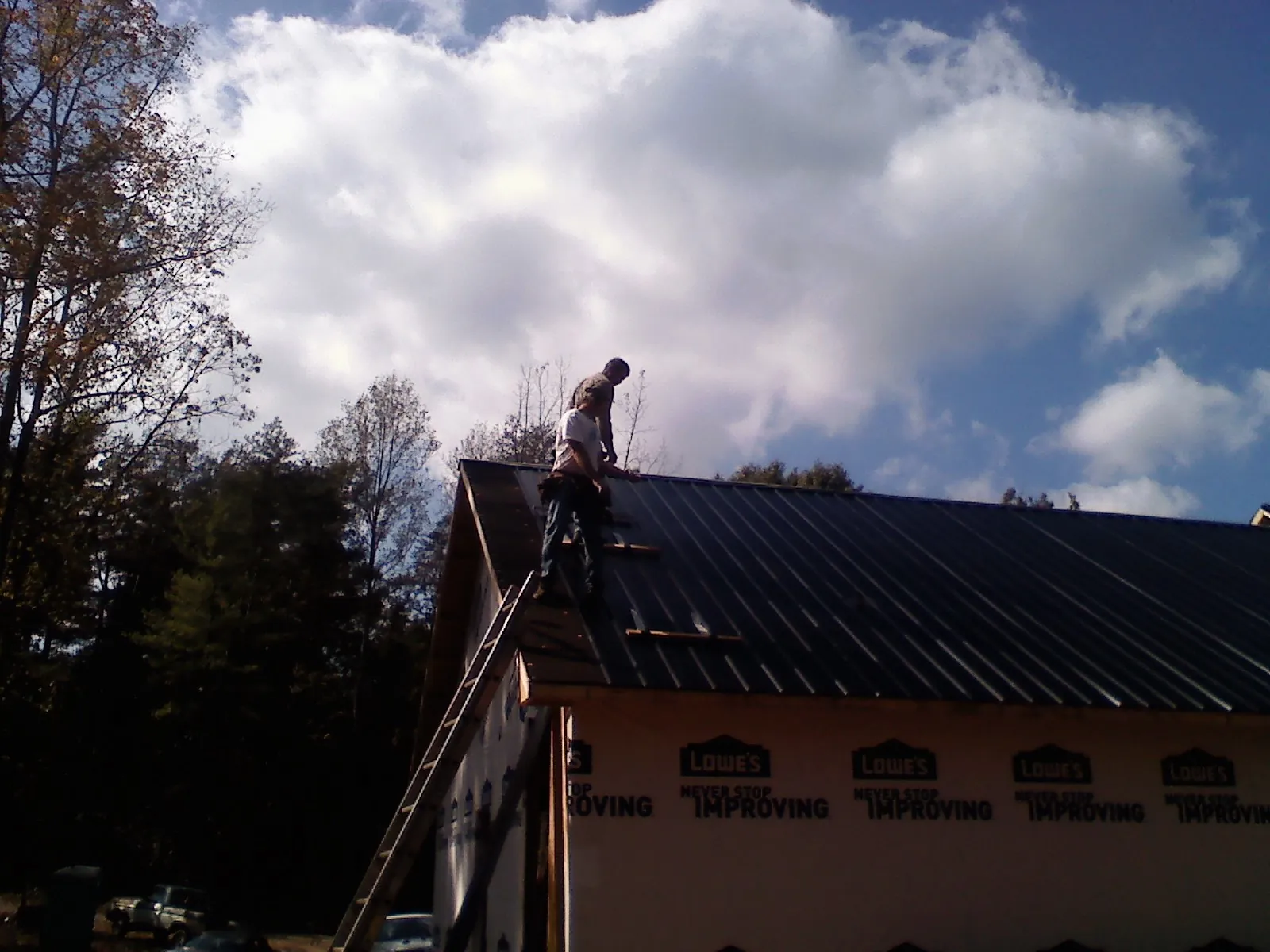 Roofer fastening dark metal panels high against a cloudy sky, from a Roof Inspection job in Bogart