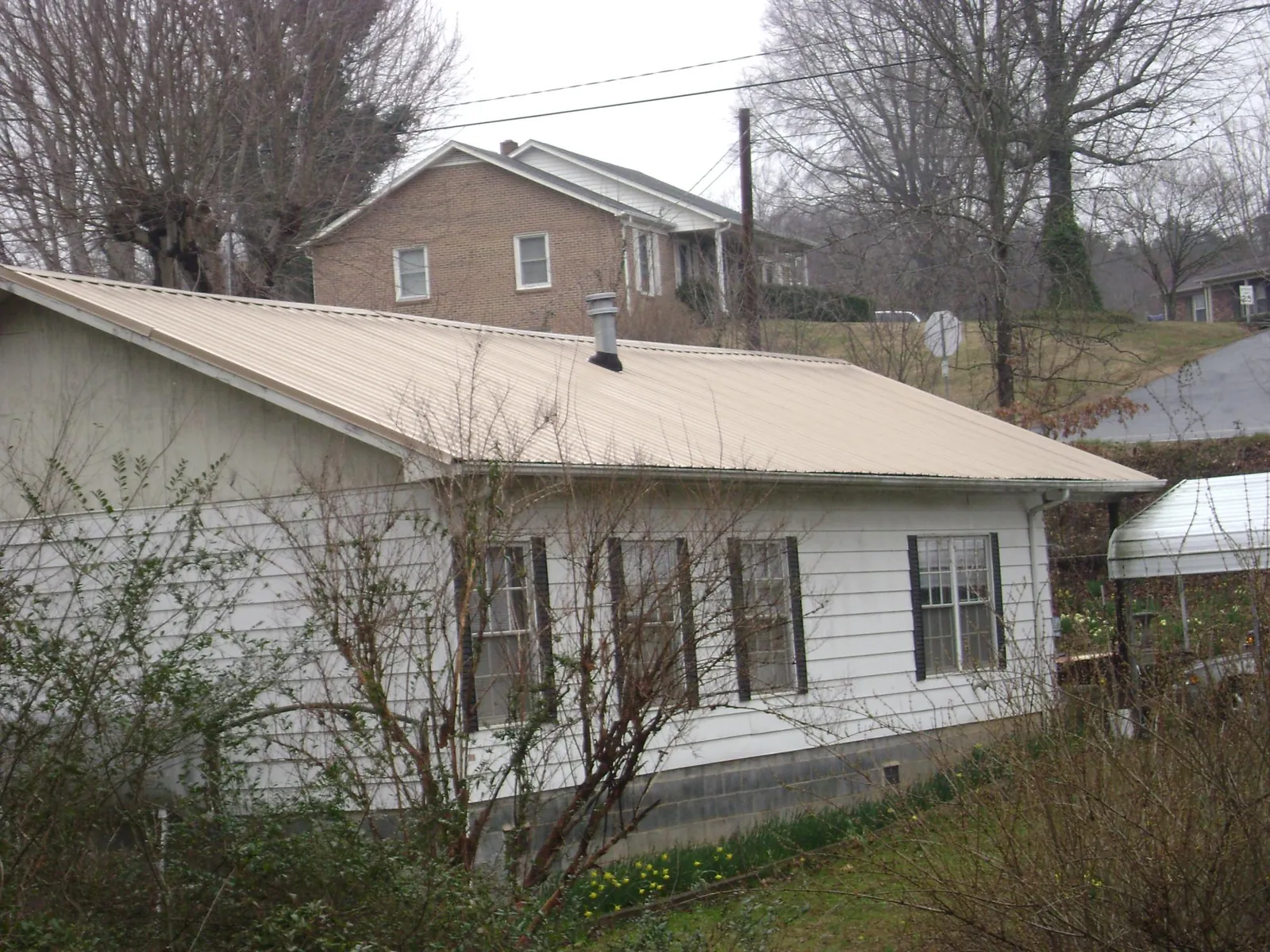 Tan metal roof on a white sided house set into a hillside — Commercial Roofing by Roofing Brothers in Bogart
